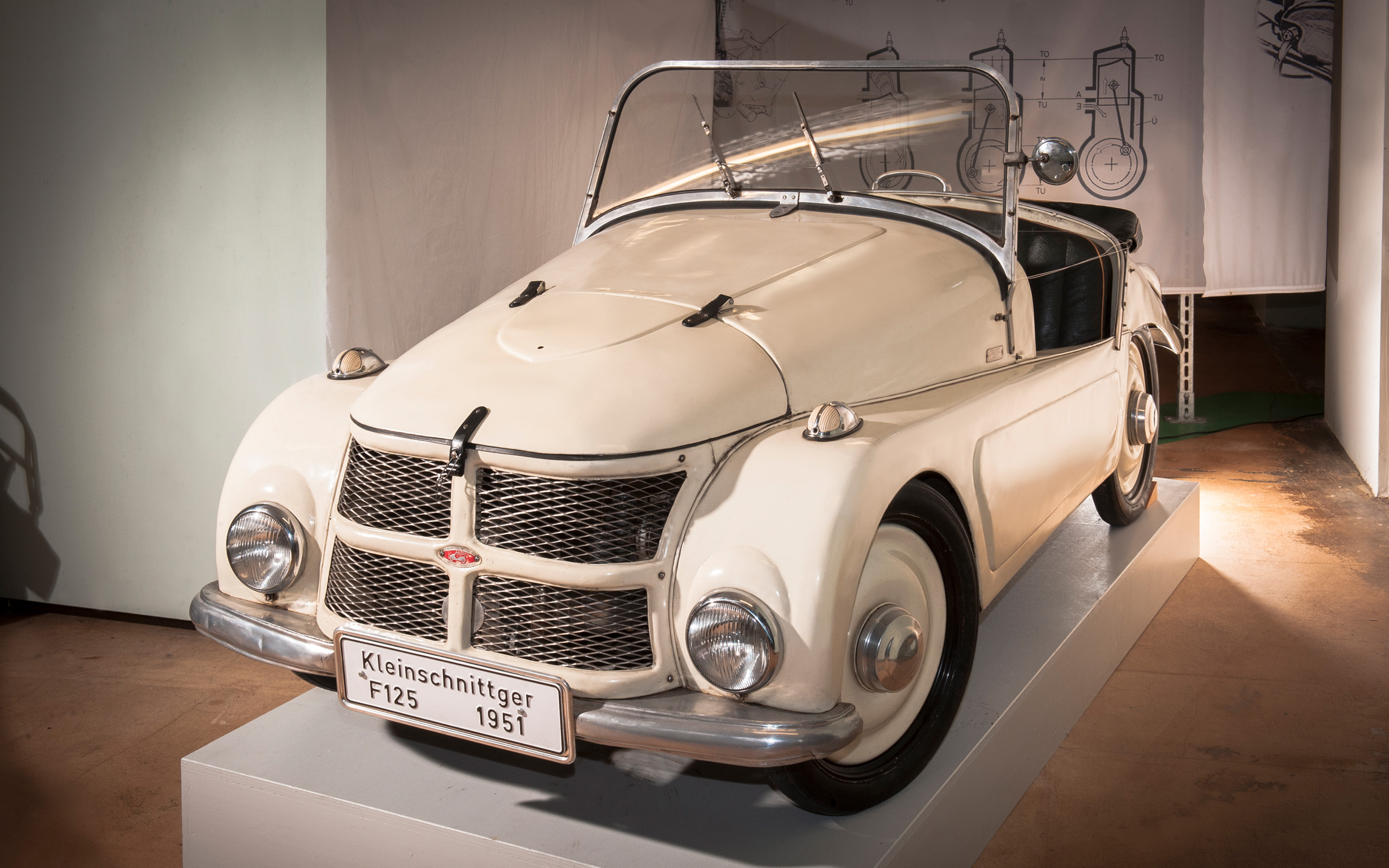 Ein historisches Fahrzeug, der Kleinschnittger F125 von 1951, steht auf einer weißen Podest. Der Wagen hat eine helle Lackierung und ein offenes Verdeck. Die Front zeigt einen markanten Kühlergrill und runde Scheinwerfer. Ein Typenschild mit der Bezeichnung ist sichtbar.