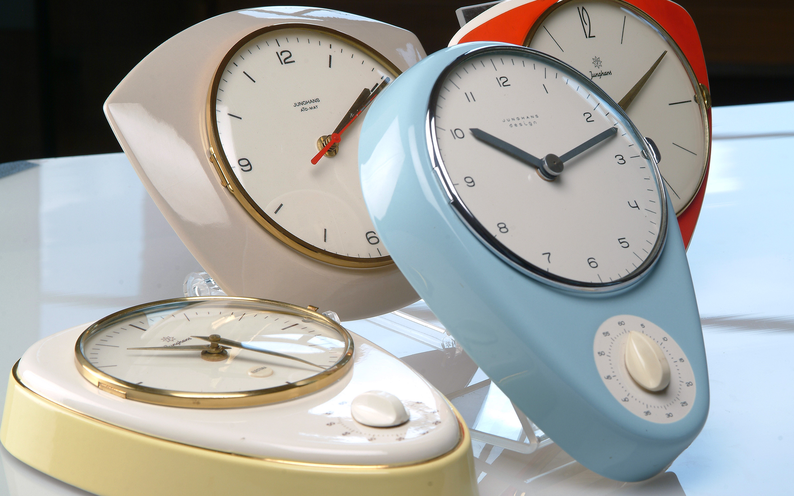 Vier verschiedene Küchenuhren stehen auf einem Tisch. Die Uhren haben unterschiedliche Farben und Designs: eine beige, eine rote, eine blaue und eine weiße Uhr. Die Ziffern sind klar ablesbar, und einige haben einen zusätzlichen Drehknopf. Sie wirken modern und dekorativ.